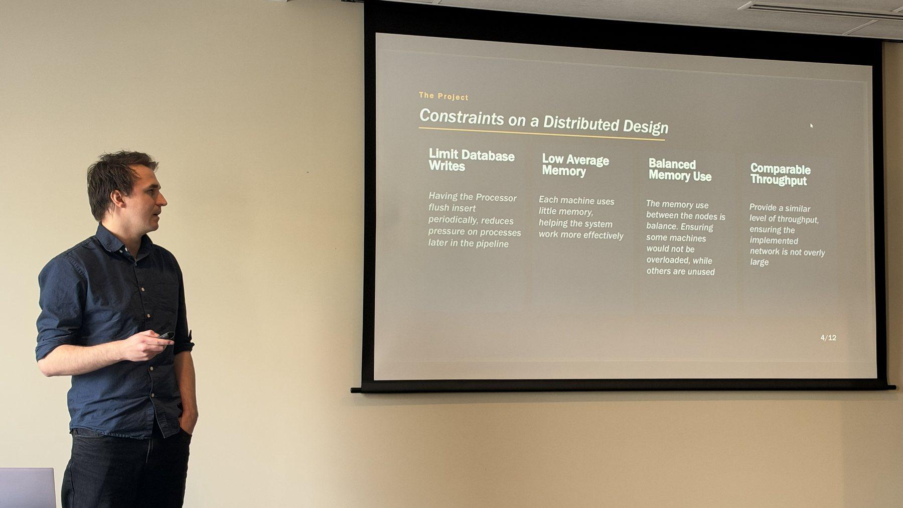 Dylan Costello presents a slide titled “Constraints on a Distributed Design”, with four columns: limit database writes, low average memory, balanced memory use and comparable throughput.
